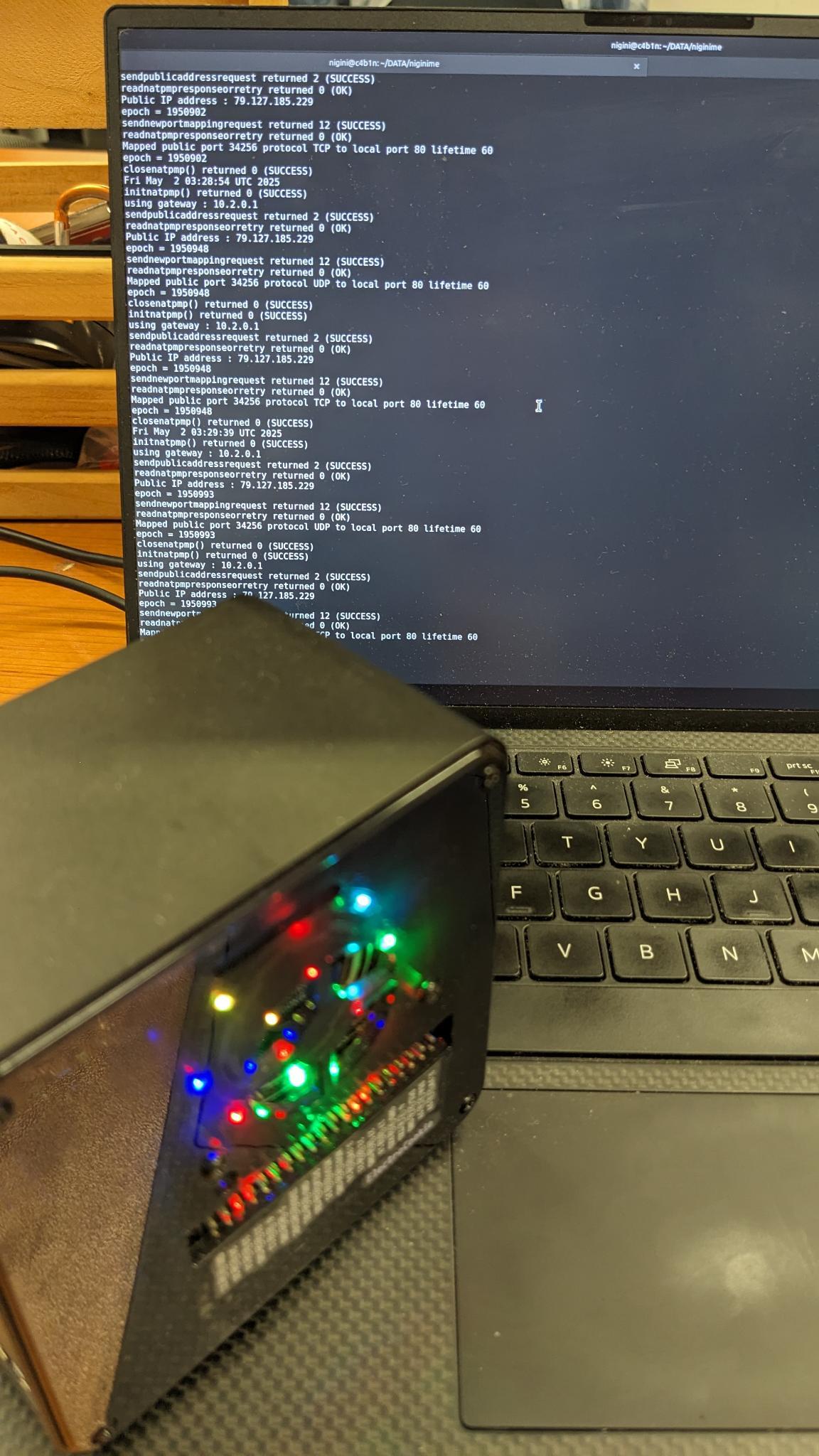 A photograph of a tiny computer tower with a Raspberry Pi 4 inside, in front of a screen showing some terminal logs.